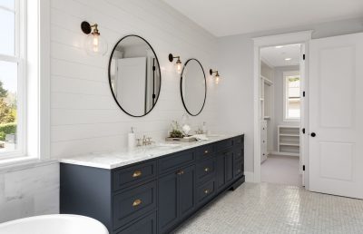Beautiful-White-and-Bright-Bathroom-in-New-Luxury-Home-with-Large-Vanity-and-Dark-Blue-Cabinets.Features-Bathtub-and-Two-Sinks,-and-Circular-Mirrors